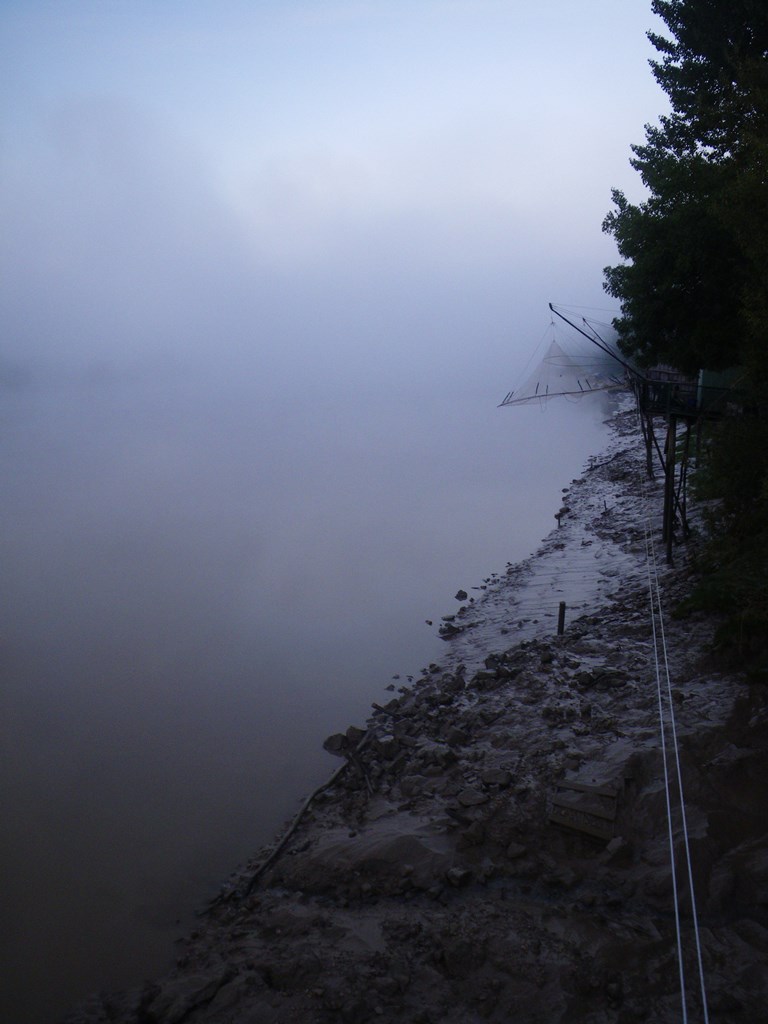 Nets hang above riverside mud in fog